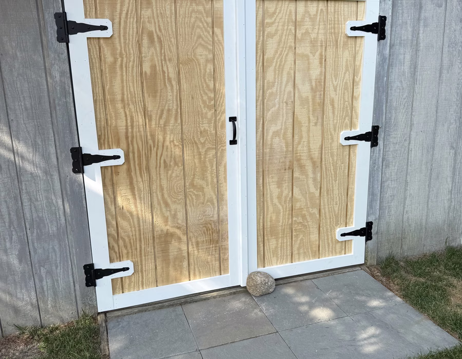 Shed doors with wood panels, white trim, and black strap hinges