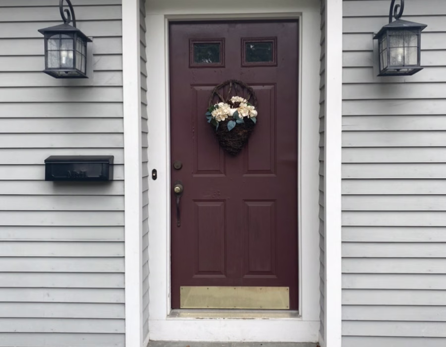 Front entry with a burgundy door, wreath, and brass kick plate